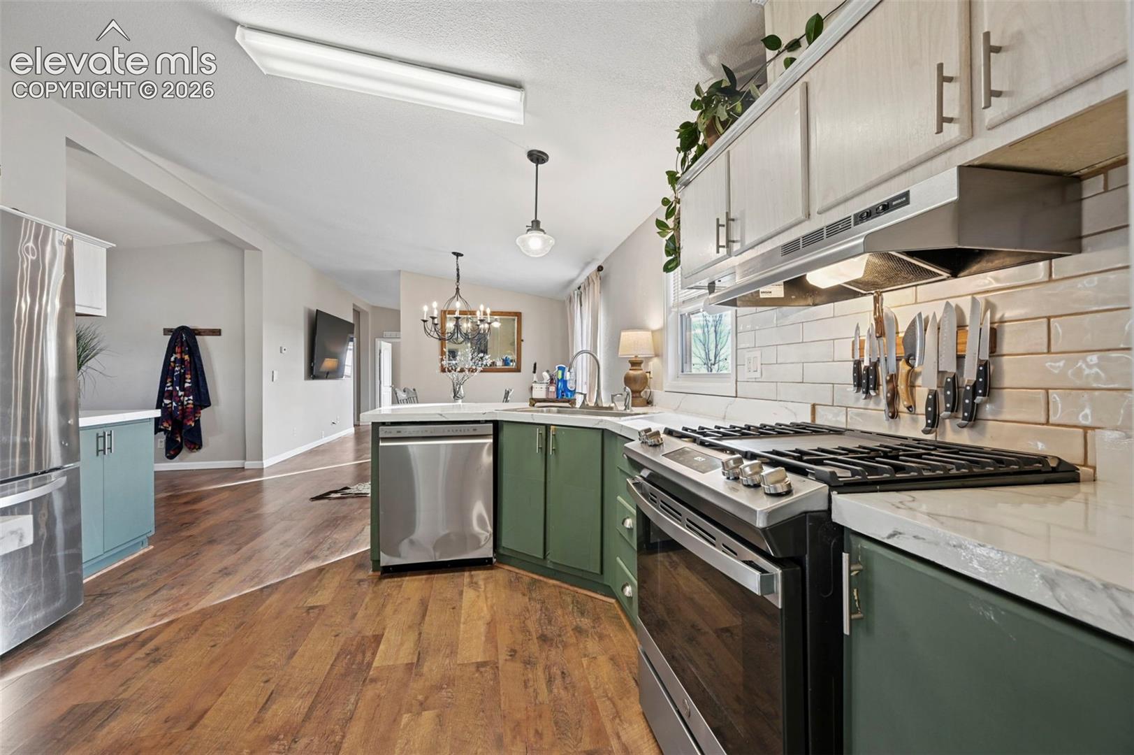 Kitchen featuring two-tone cabinetry, stainless steel appliances, light-toned stone-surface countertops, subway tile backsplash, and wood-finish flooring