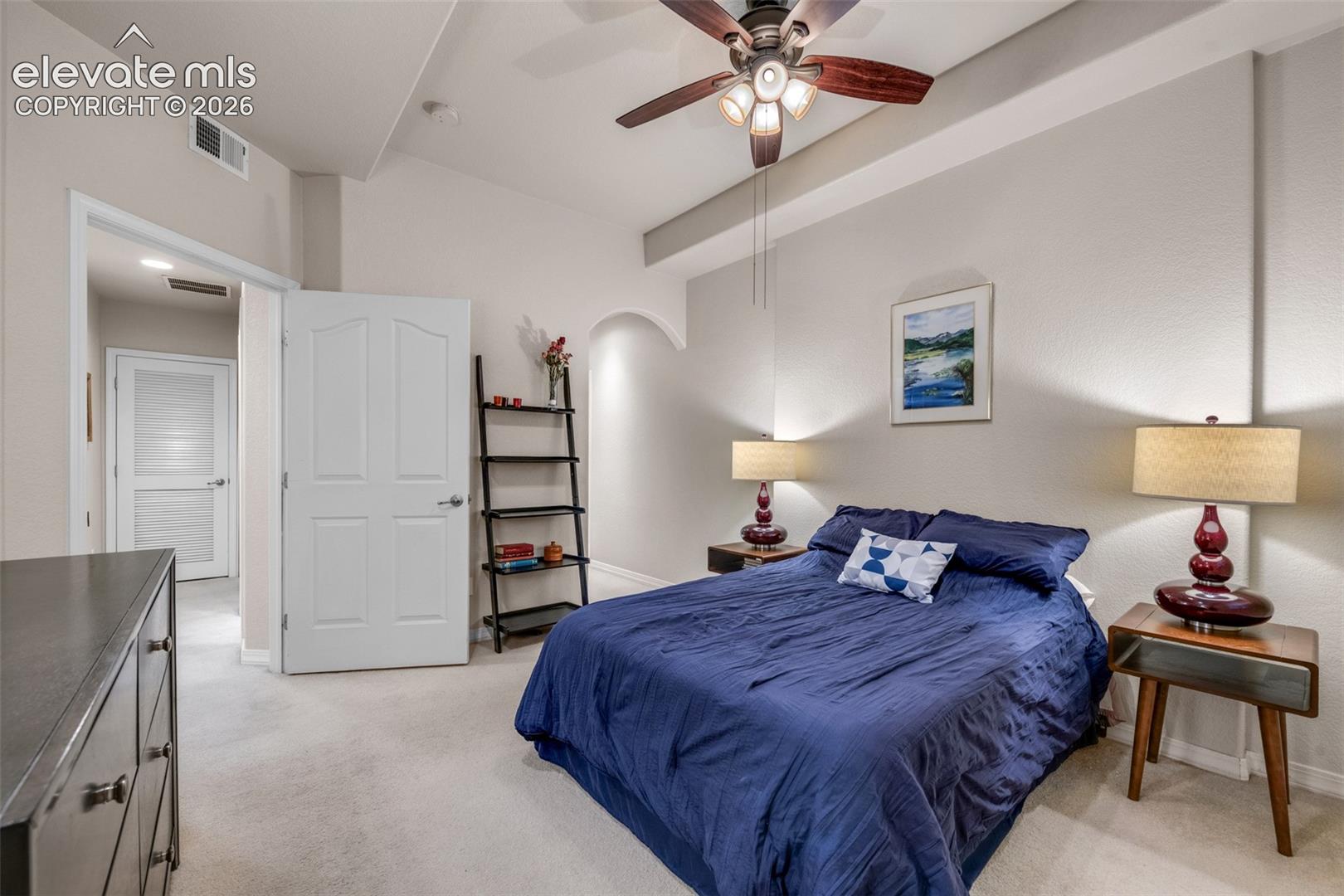 Vaulted ceiling with an integrated ceiling fan, arched wall recess, and light-toned carpeting