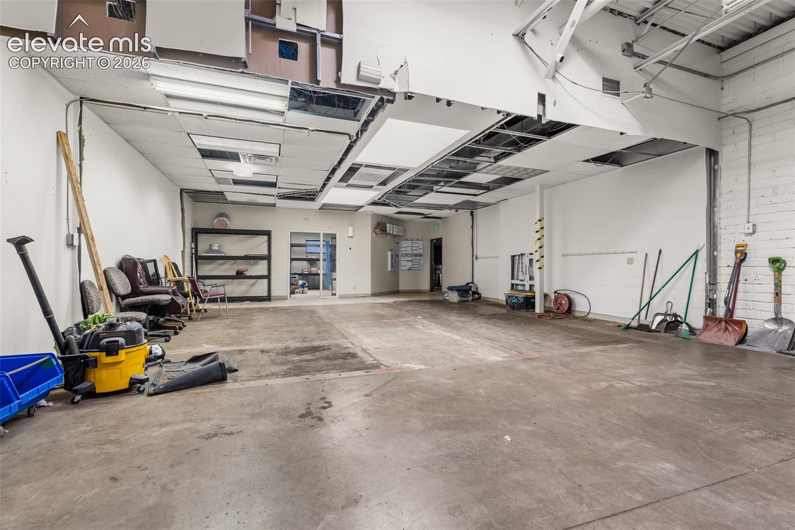 Open-concept industrial workspace featuring concrete flooring, exposed ceiling components, and painted brick walls