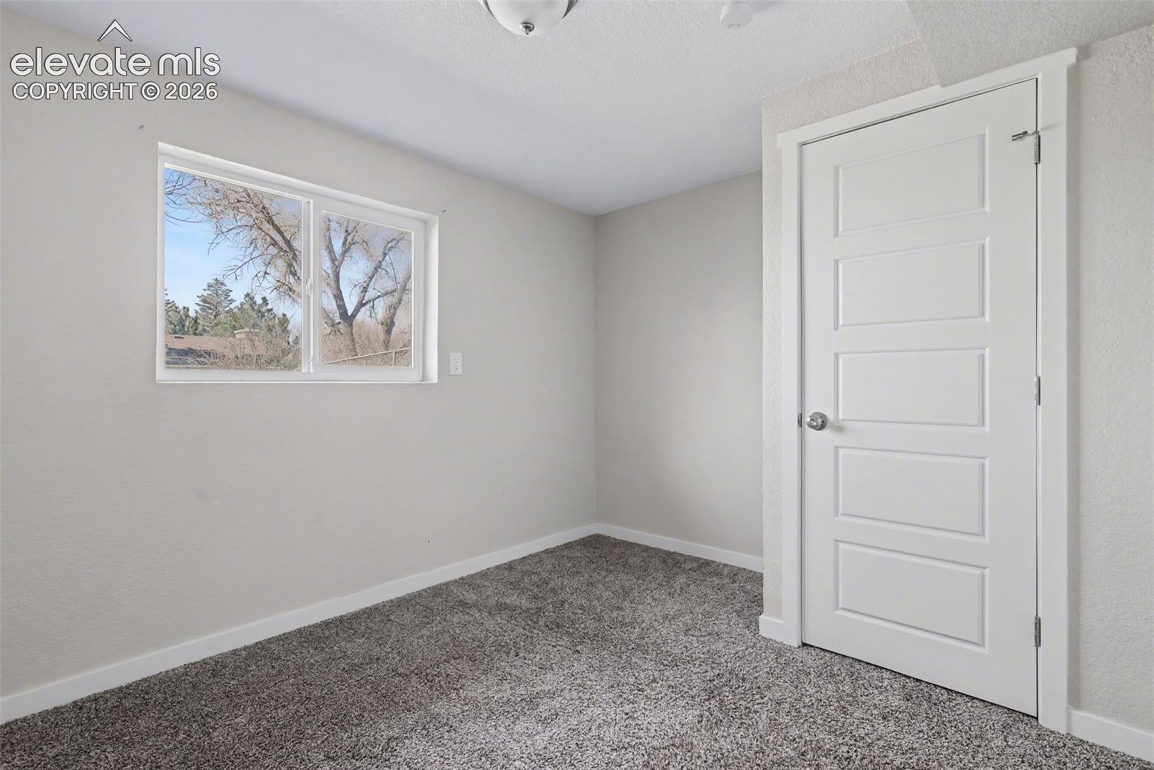 Neutral-toned room featuring textured wall-to-wall carpeting, a five-panel interior door with brushed metal hardware, and a horizontal sliding window