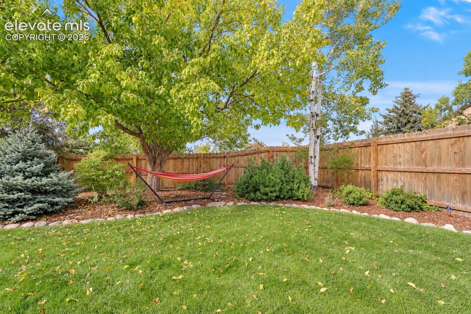 Private backyard featuring mature trees, a wooden perimeter fence, stone landscape edging, and manicured lawn, greenway behind fence adds privacy