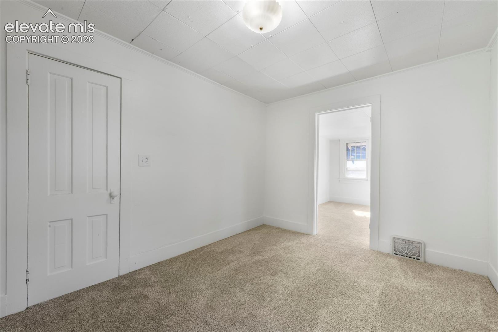Neutral-toned wall-to-wall carpeting, white four-panel interior door, ceiling-mounted dome light fixture, and tile-finish ceiling panels