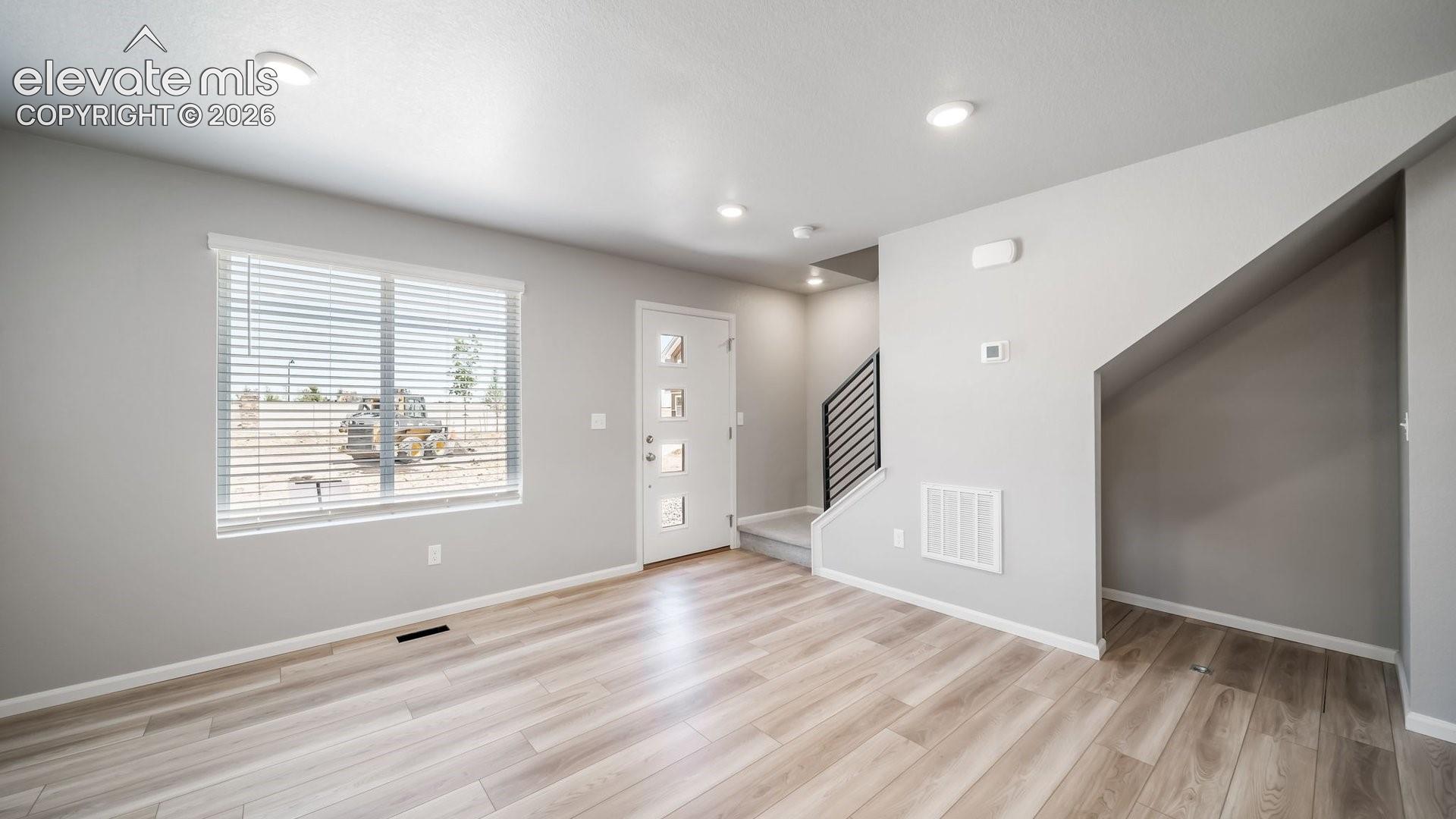 Wood-finish flooring, recessed lighting, white entry door with four glass panels, and metal baluster staircase railing
*photos of a model home*