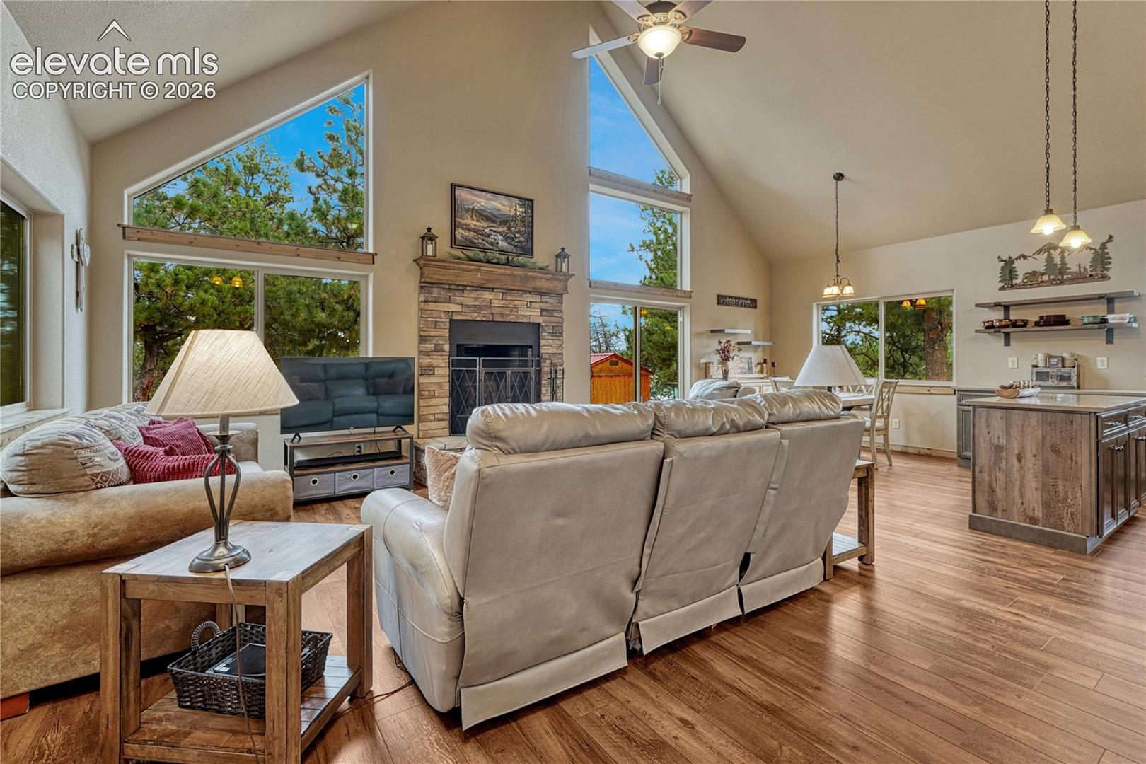 Vaulted ceilings featuring expansive geometric windows, natural stone-faced fireplace with wood mantel, and wood-finish flooring