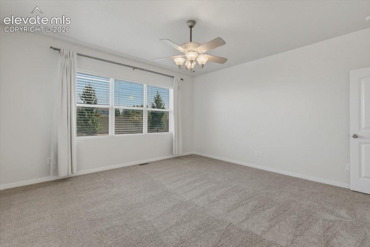 Spacious room featuring neutral carpeting, a multi-pane window with blinds, a ceiling fan with integrated lighting, and a paneled interior door