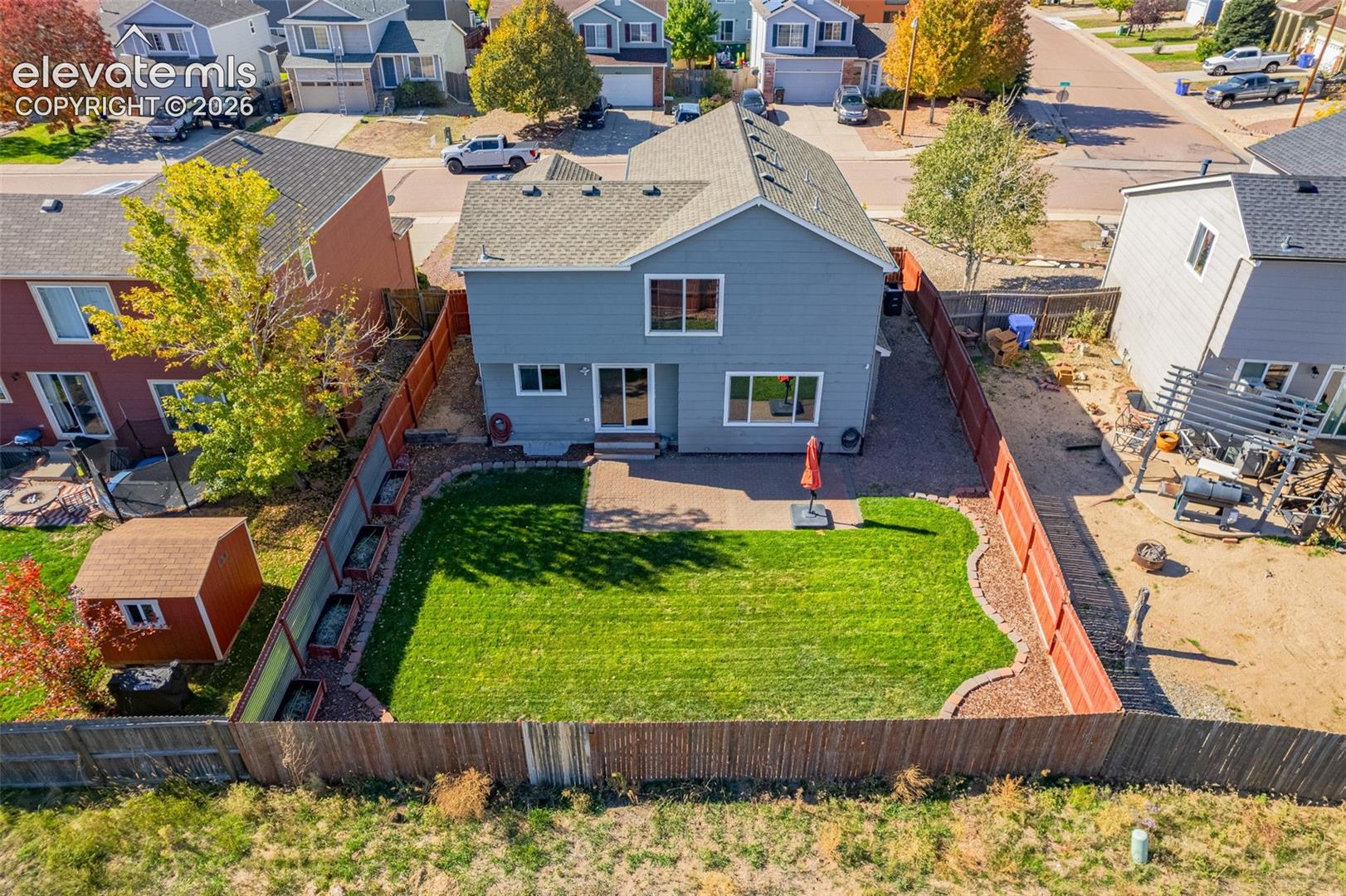 Two-story residence featuring grey lap siding, a fenced backyard, a manicured lawn, a concrete patio, and an external storage structure