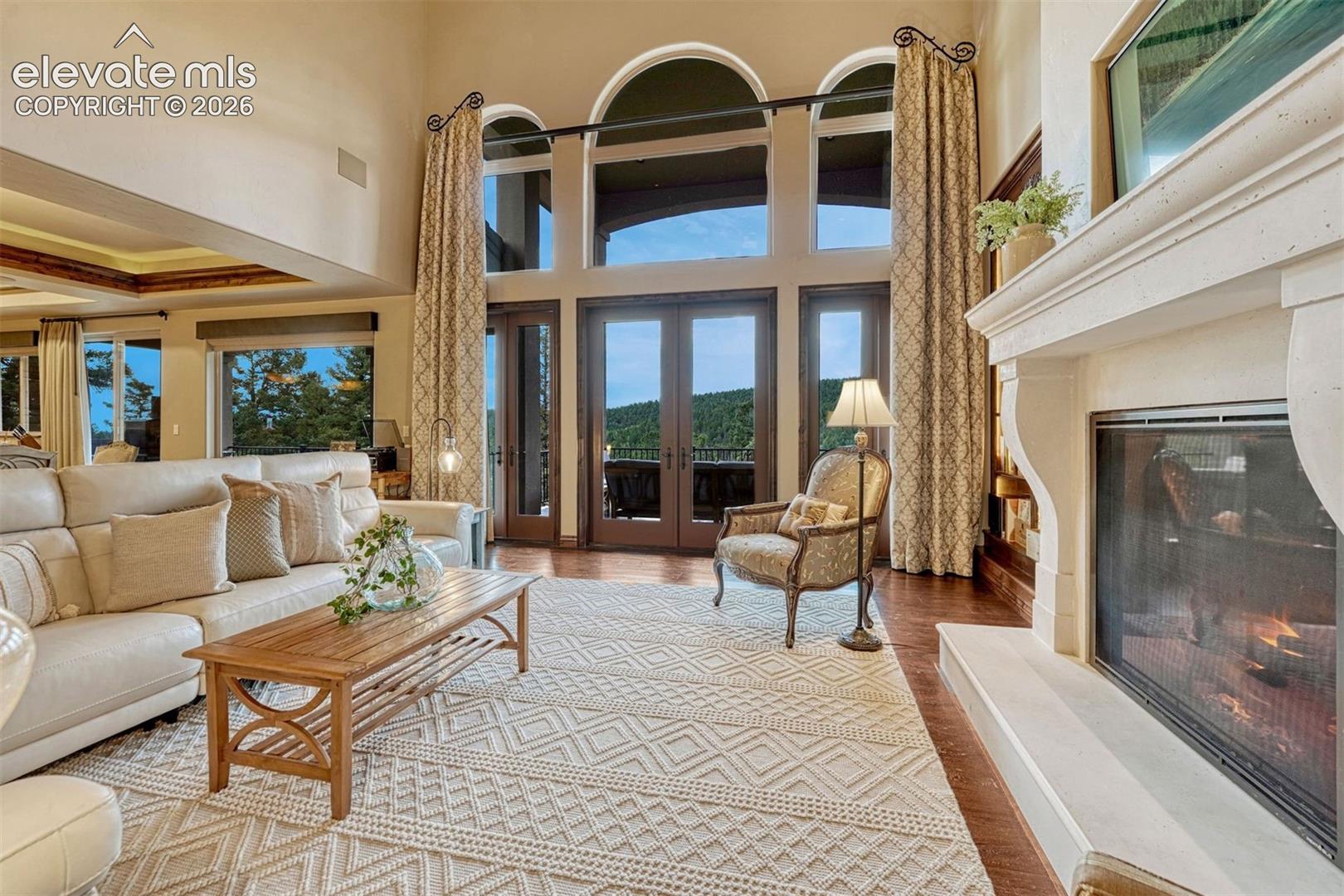 Two-story living area with hardwood flooring, a stone-clad fireplace, and arched windows and doors