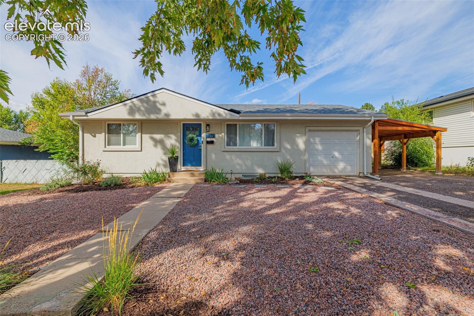Single-story stucco exterior with an attached garage, a carport, and a blue entry door
