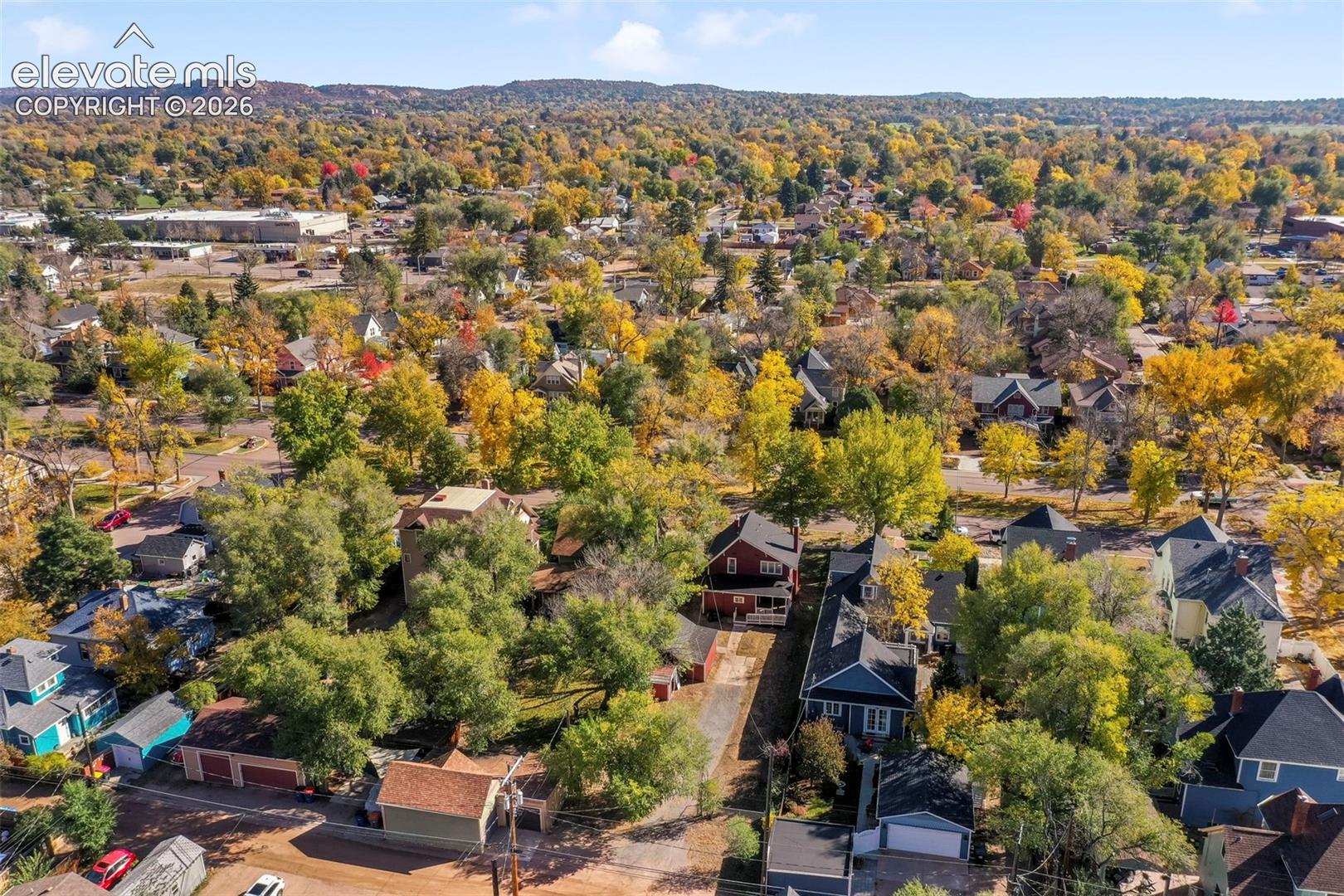 Aerial perspective of a residential neighborhood featuring mature trees, diverse building styles, paved streets, and a mountainous horizon