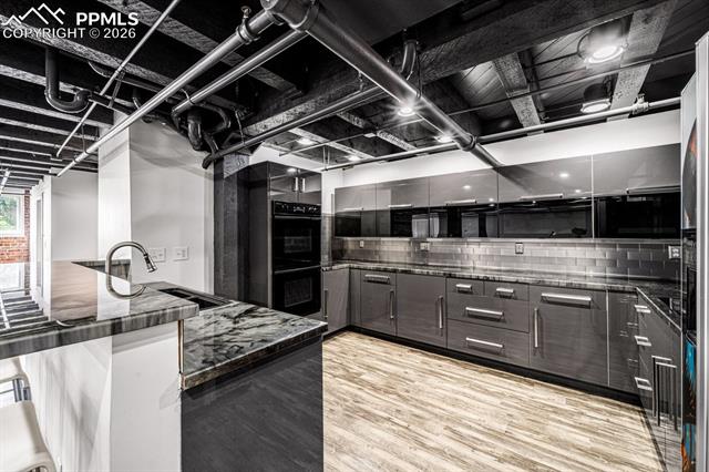 Kitchen featuring light wood-style floors, decorative backsplash, modern cabinets, and dark stone countertops