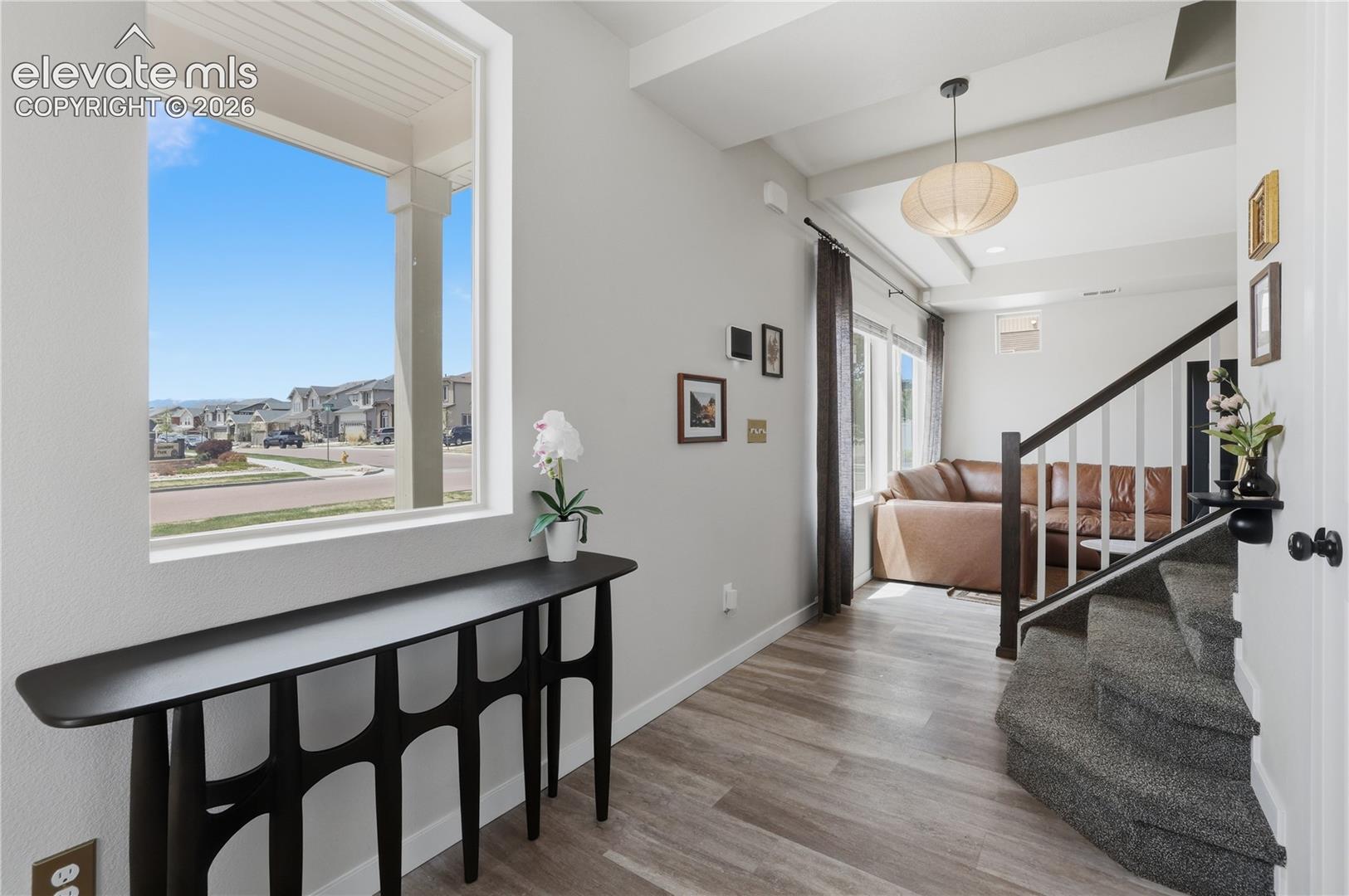 Bright entryway featuring a large window, wood-finish flooring, and exposed ceiling beams