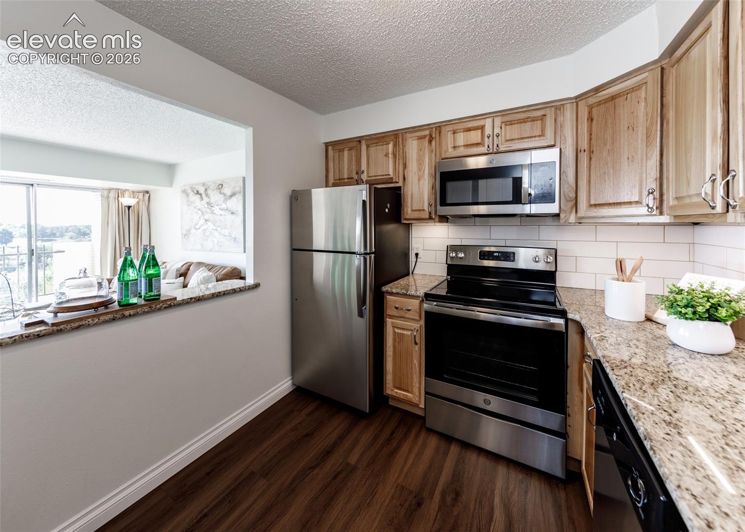 Kitchen featuring wood-finish cabinetry, natural stone-patterned countertops, stainless steel appliances, subway tile backsplash, and wood-finish flooring