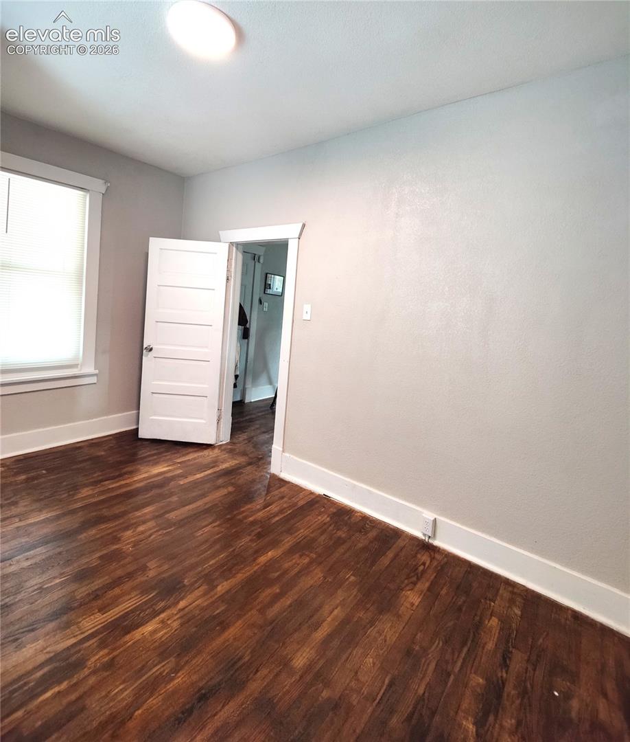 Rich wood-finish flooring with white trim, a flush-mount ceiling light, and a paneled interior door
