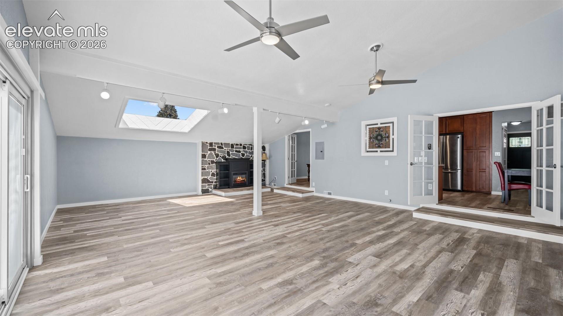 Spacious living area featuring wood-finish flooring, a stone-front fireplace, and vaulted ceilings with dual ceiling fans