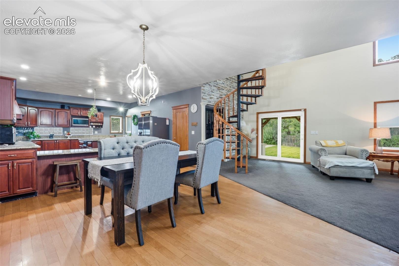 Wood-finish flooring, cherry wood cabinetry with stone countertops, a spiral staircase with wood railing, high ceilings, and sliding glass doors to the exterior