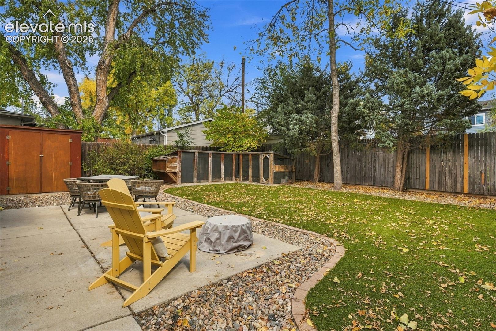 Private backyard featuring a concrete patio, synthetic turf lawn, perimeter wood fencing, and an enclosed exterior structure