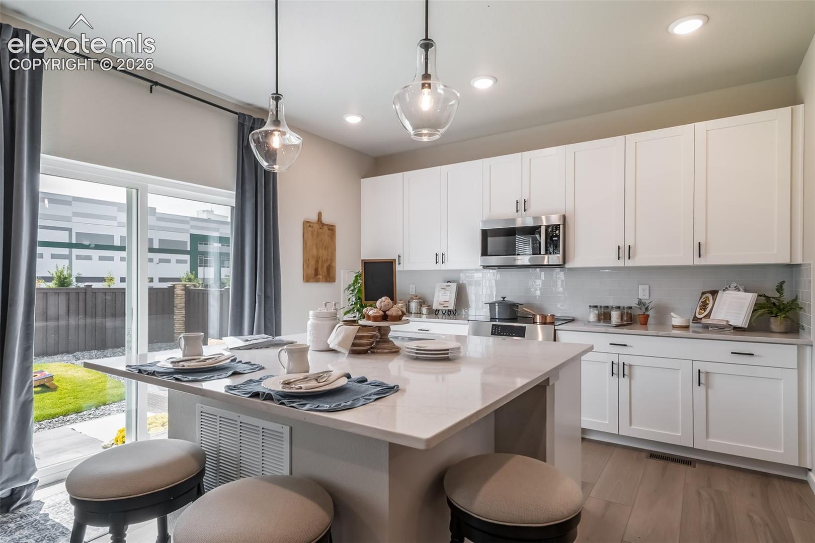 Kitchen featuring a central island with countertop seating, white shaker-style cabinetry, stainless steel appliances, and a tile backsplash
*Photos of a model home*