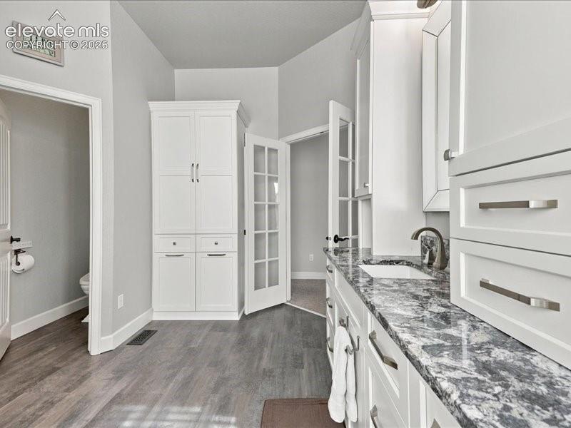 White cabinetry with brushed nickel hardware, expansive countertop with an undermount sink, wood-finish flooring, and a built-in storage cabinet