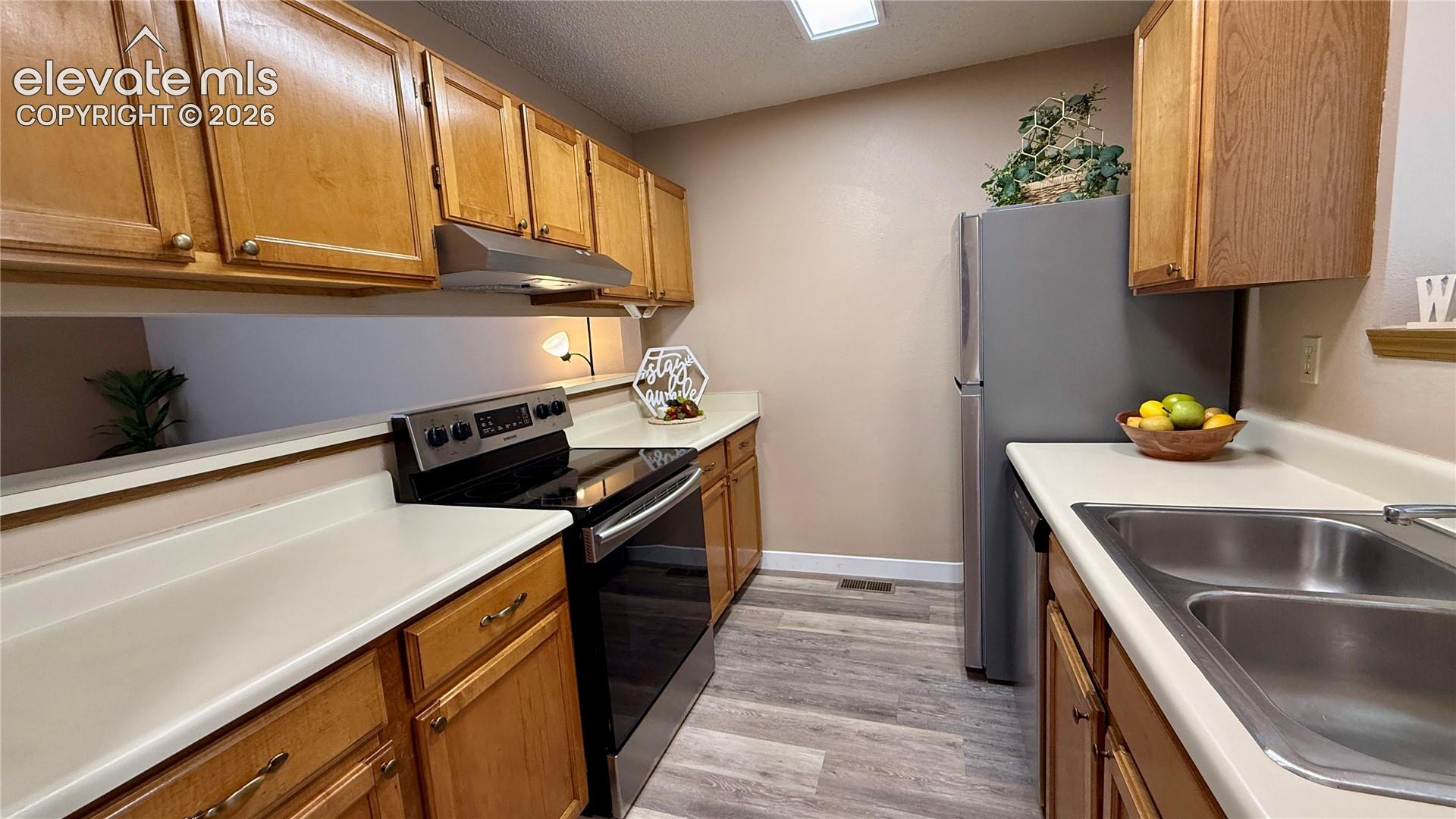 Kitchen featuring wood-look cabinetry, light colored countertops, wood-look flooring, and NEW stainless steel appliances including a range and refrigerator