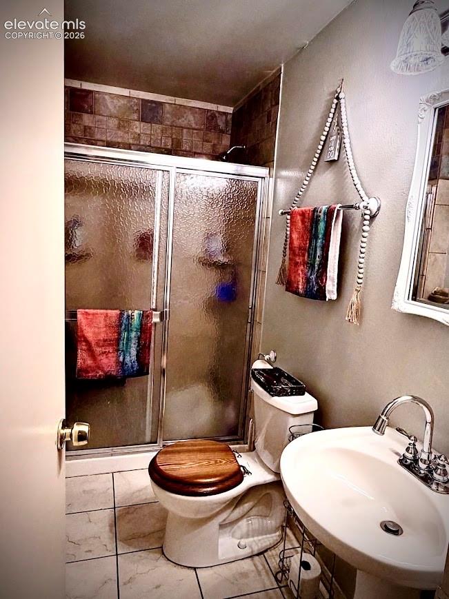 Lower level bathroom featuring a tiled walk-in shower with sliding glass doors, a vanity with an integrated sink, a two-piece toilet with a wood-finish seat, and floor tile