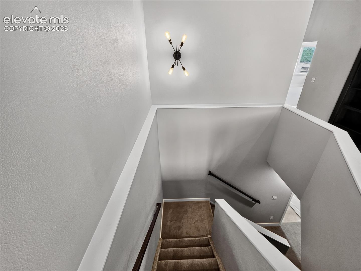 Staircase featuring textured wall finishes, a modern ceiling light fixture, neutral paint tones, and a dark wood handrail