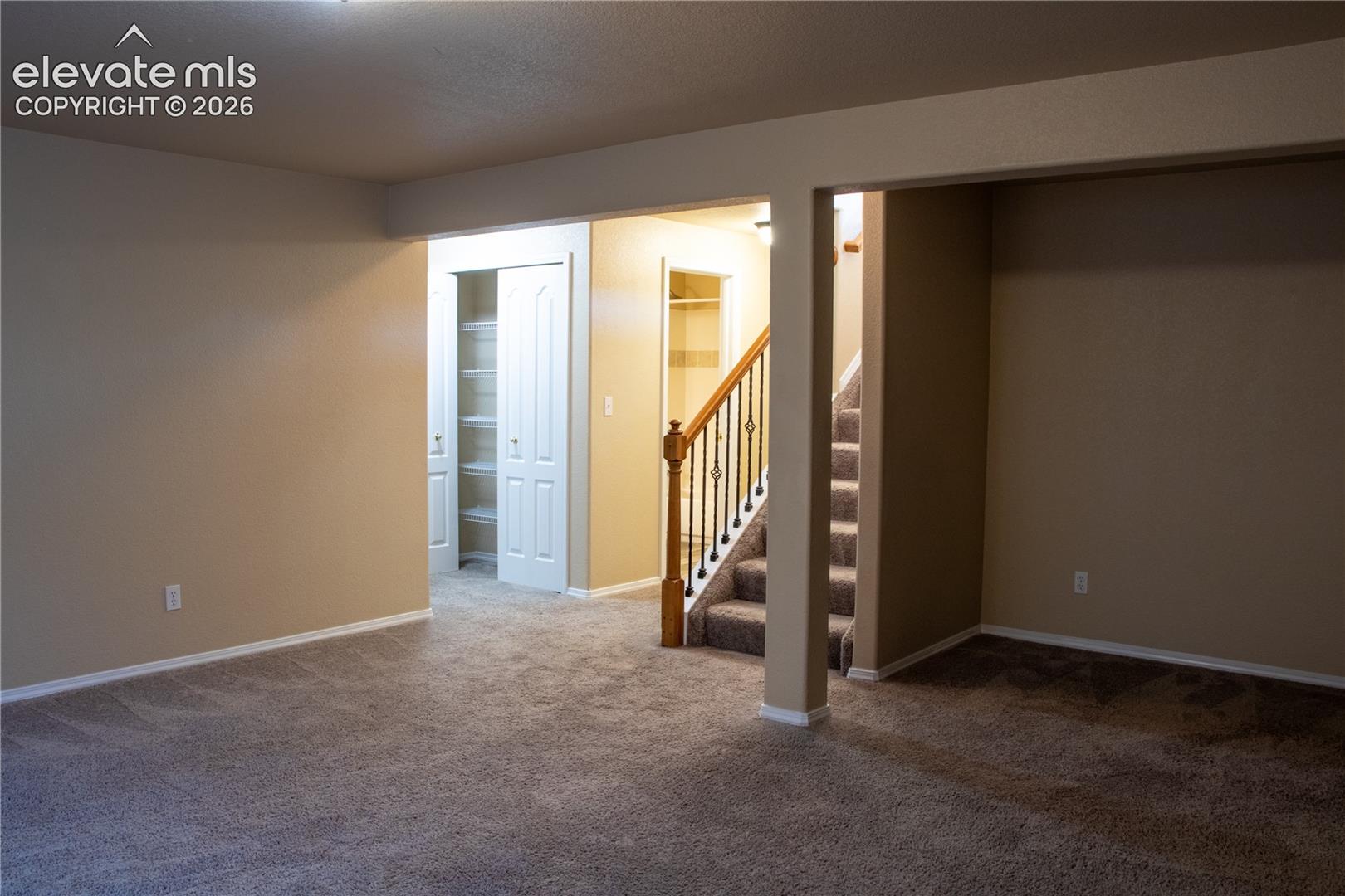 Carpeted interior space featuring neutral wall tones, white baseboards, and a staircase with wood handrail and black metal balusters