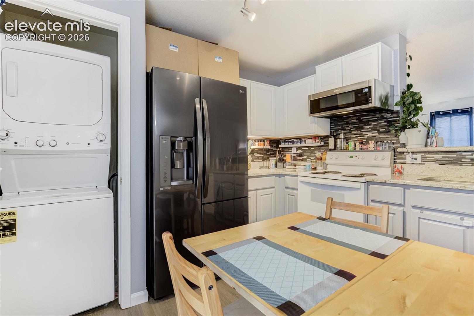 White cabinetry with a tile backsplash, stainless steel over-the-range microwave, and a dark finish refrigerator