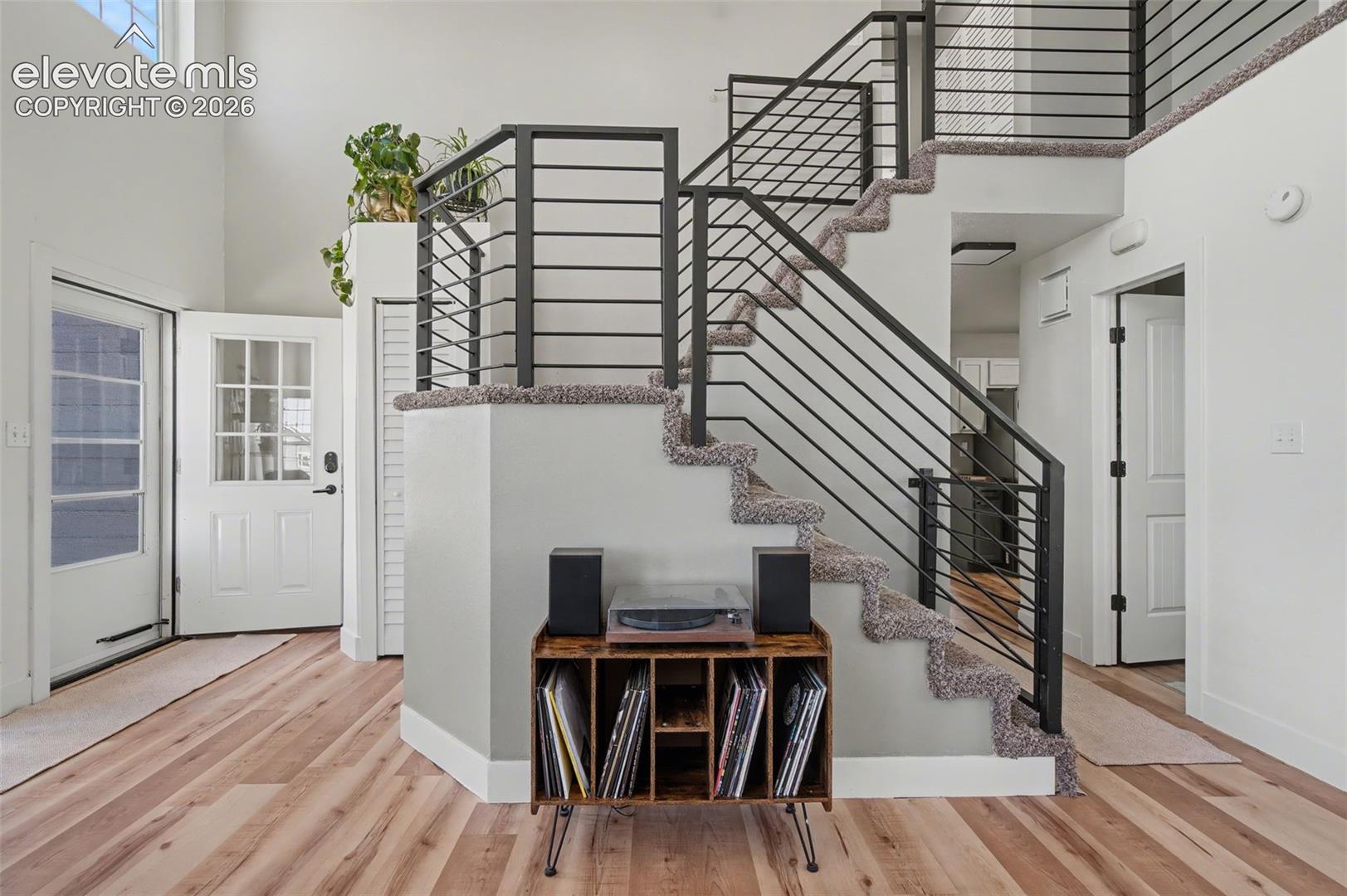 Open-concept entry featuring soaring ceilings, wood-finish flooring, and a staircase with metal horizontal railings and carpeted treads