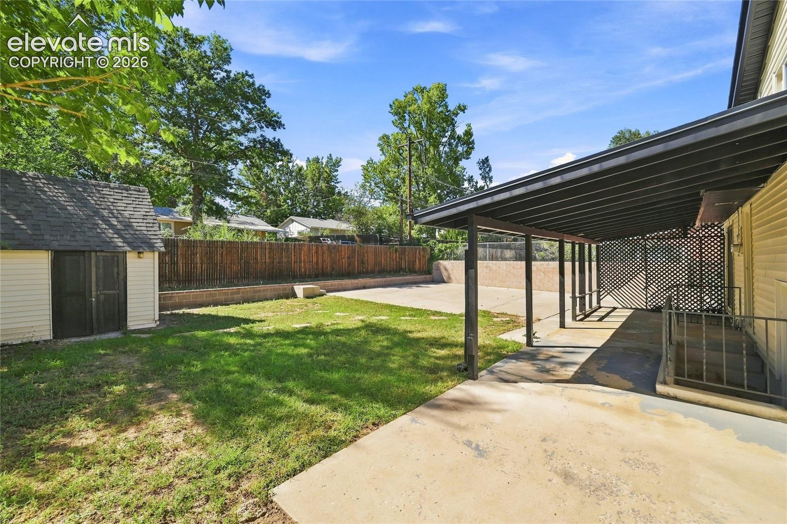 Expansive backyard featuring a storage shed, concrete patio, covered outdoor area, and wood privacy fencing