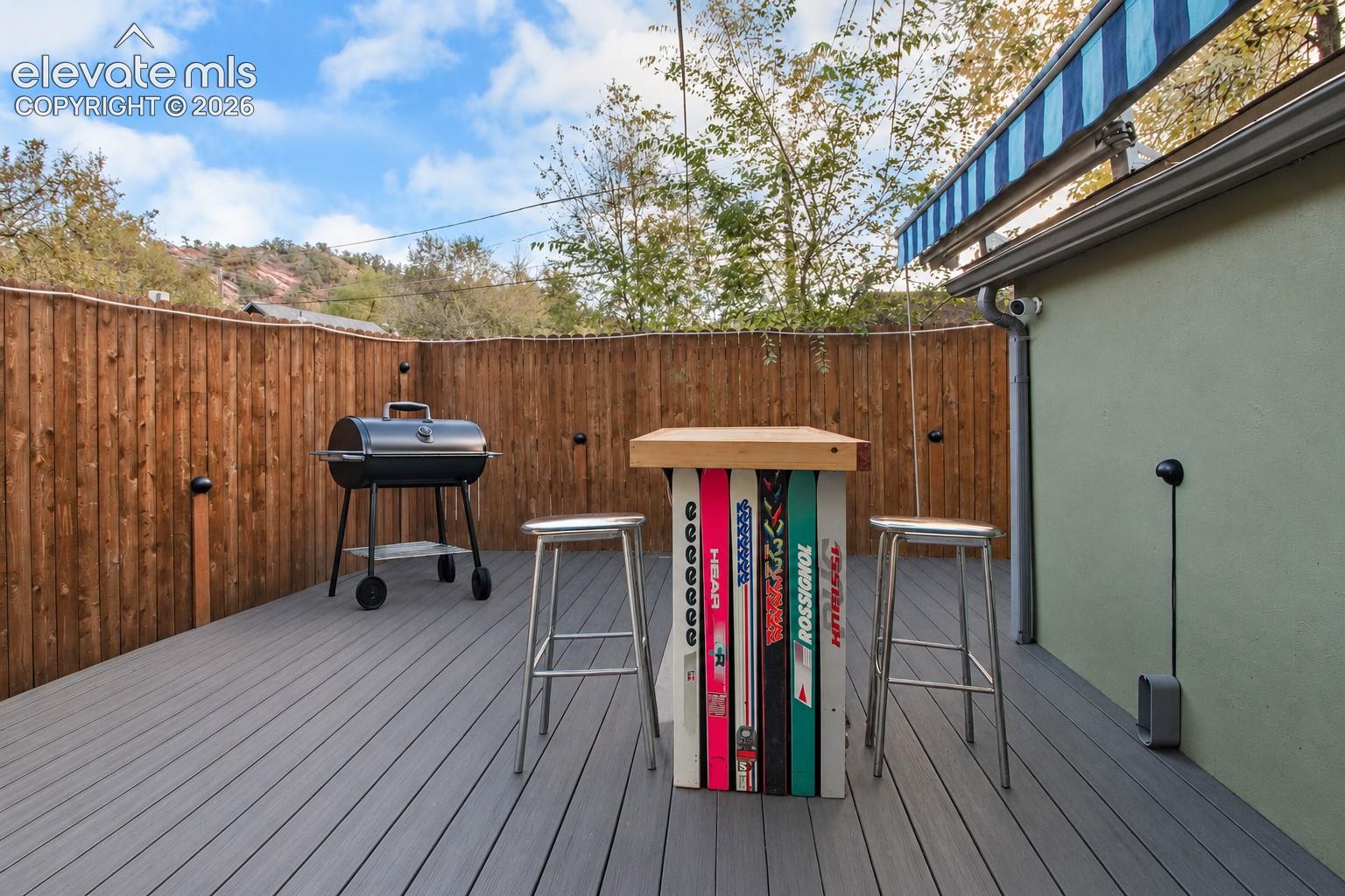 Outdoor deck featuring grey composite decking, a wood-slat privacy fence, and a retractable fabric awning