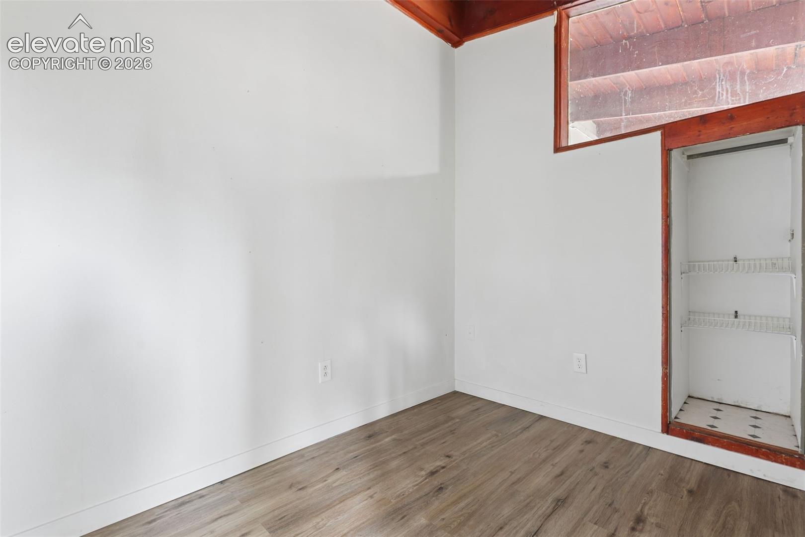 Wood-finish flooring, white walls, built-in shelving, and a wood-framed window