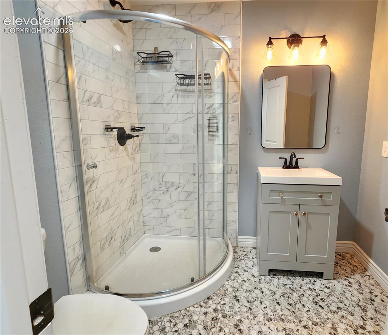 Modern lower-level bathroom boasting a premium corner glass shower and patterned tile floors