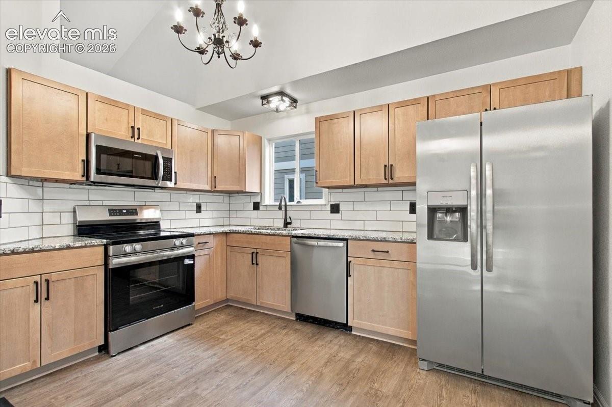 Kitchen featuring light-finish cabinetry, stone countertops, white subway tile backsplash, stainless steel appliances, and vaulted ceiling