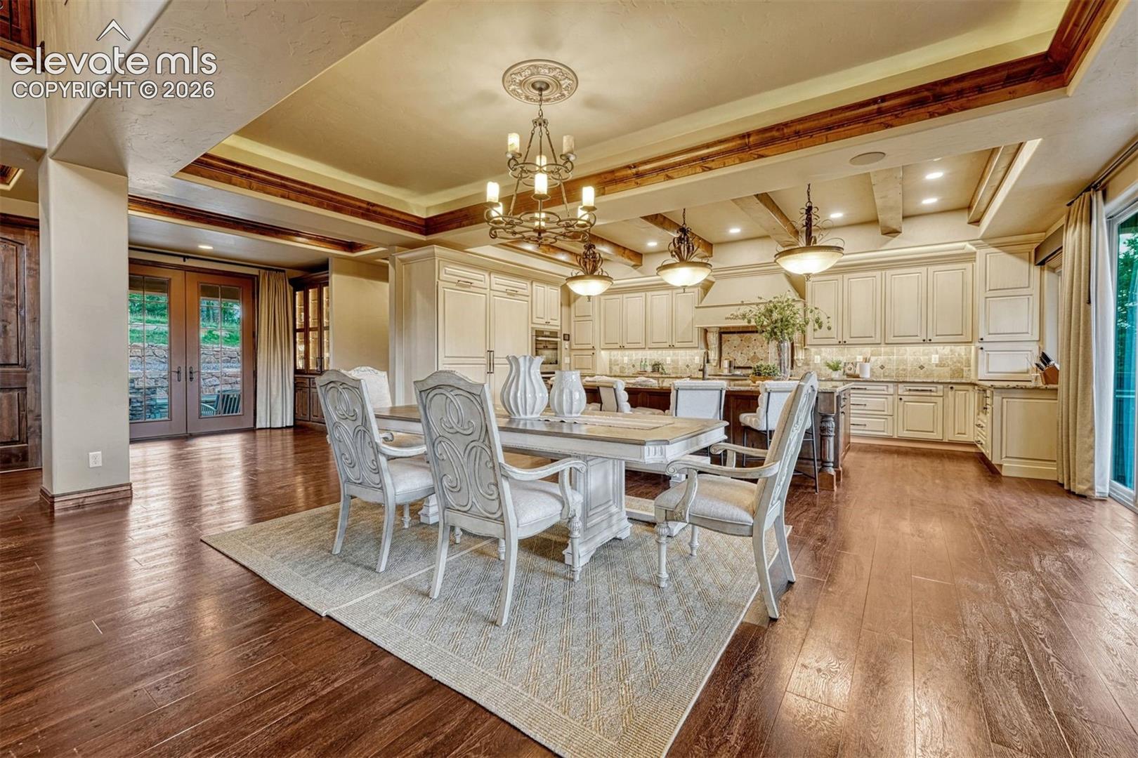 Expansive interior featuring wood-finish flooring, exposed ceiling beams, a recessed ceiling with a chandelier, and light-toned cabinetry