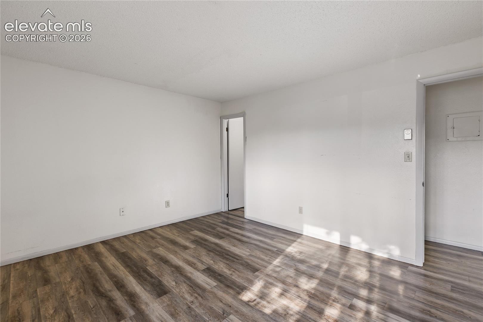 Spacious room featuring wood-finish flooring, white painted walls, and a textured ceiling