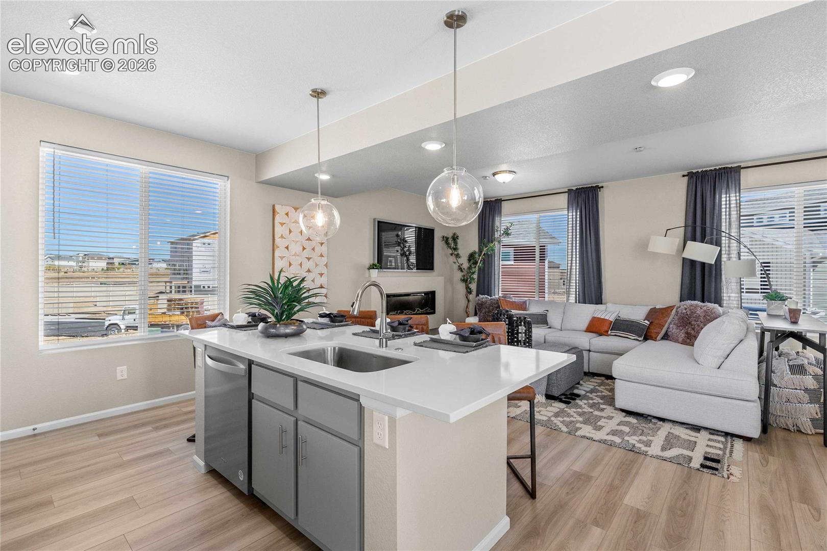 Open-concept living space featuring wood-finish flooring, recessed lighting, a kitchen island with a double basin sink and integrated dishwasher, and a built-in fireplace
*photos of a model home*