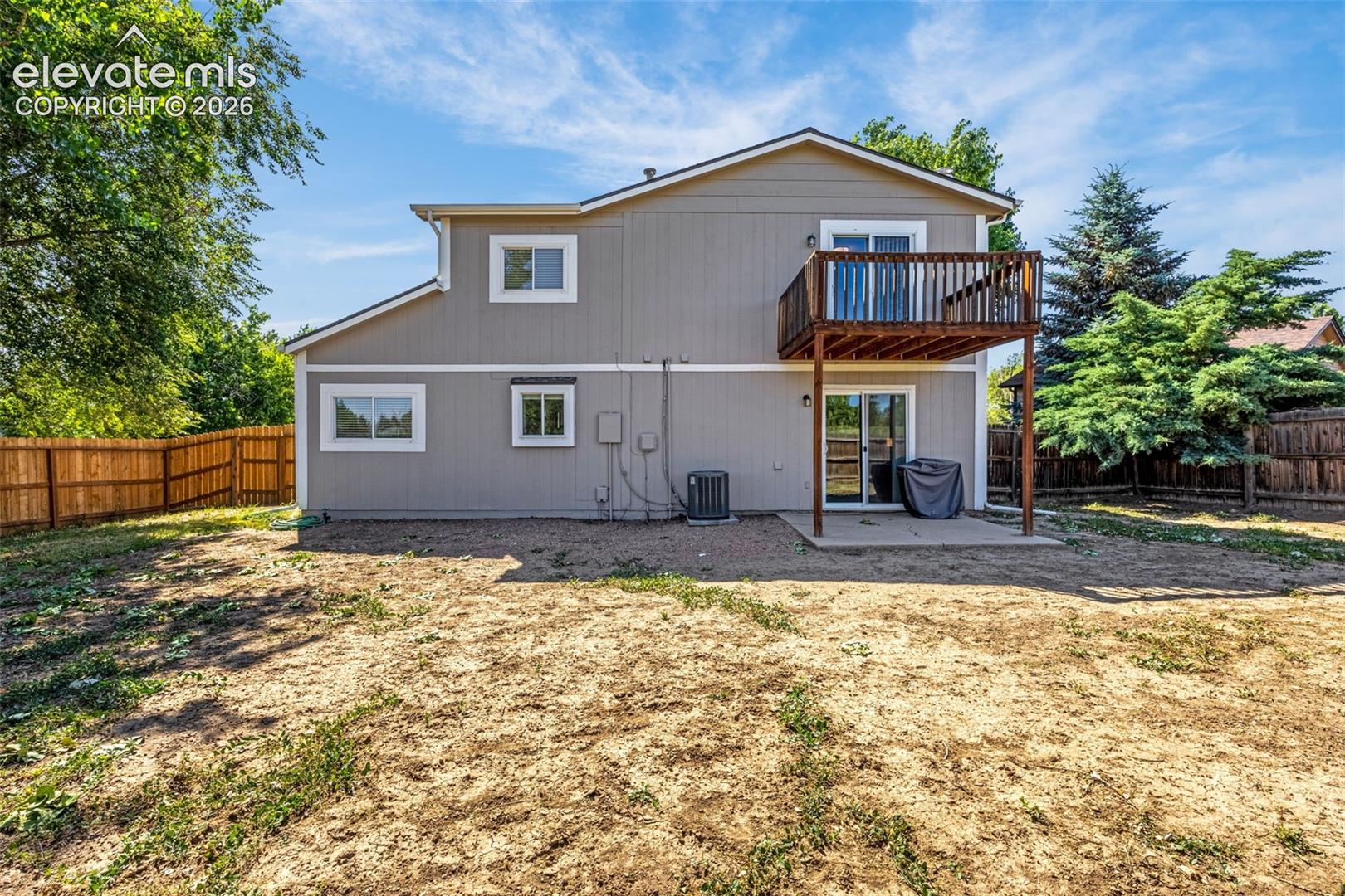 Exterior rear elevation featuring horizontal siding, a second-story wooden deck, a concrete patio, and a wood privacy fence