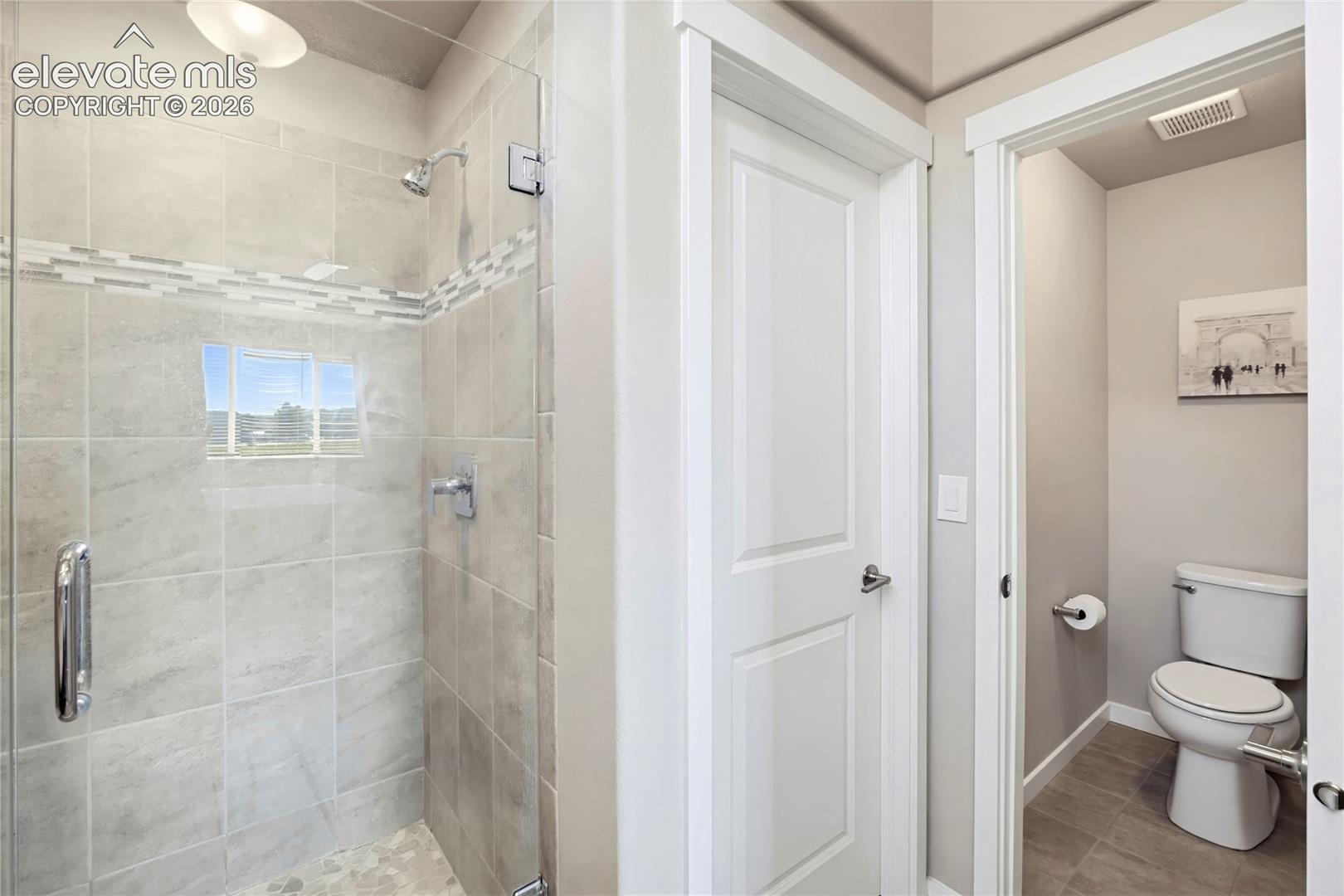 Walk-in shower with floor-to-ceiling tile, decorative mosaic inlay, glass enclosure, and polished chrome fixtures