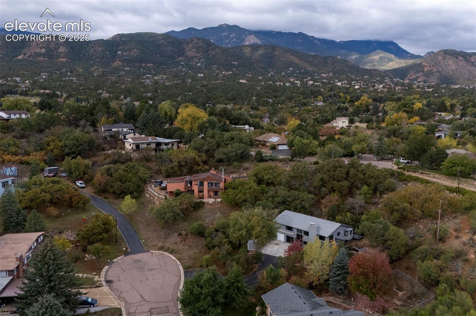 Aerial perspective featuring a hillside landscape with mountain backdrops, mature trees, and varied residential architecture