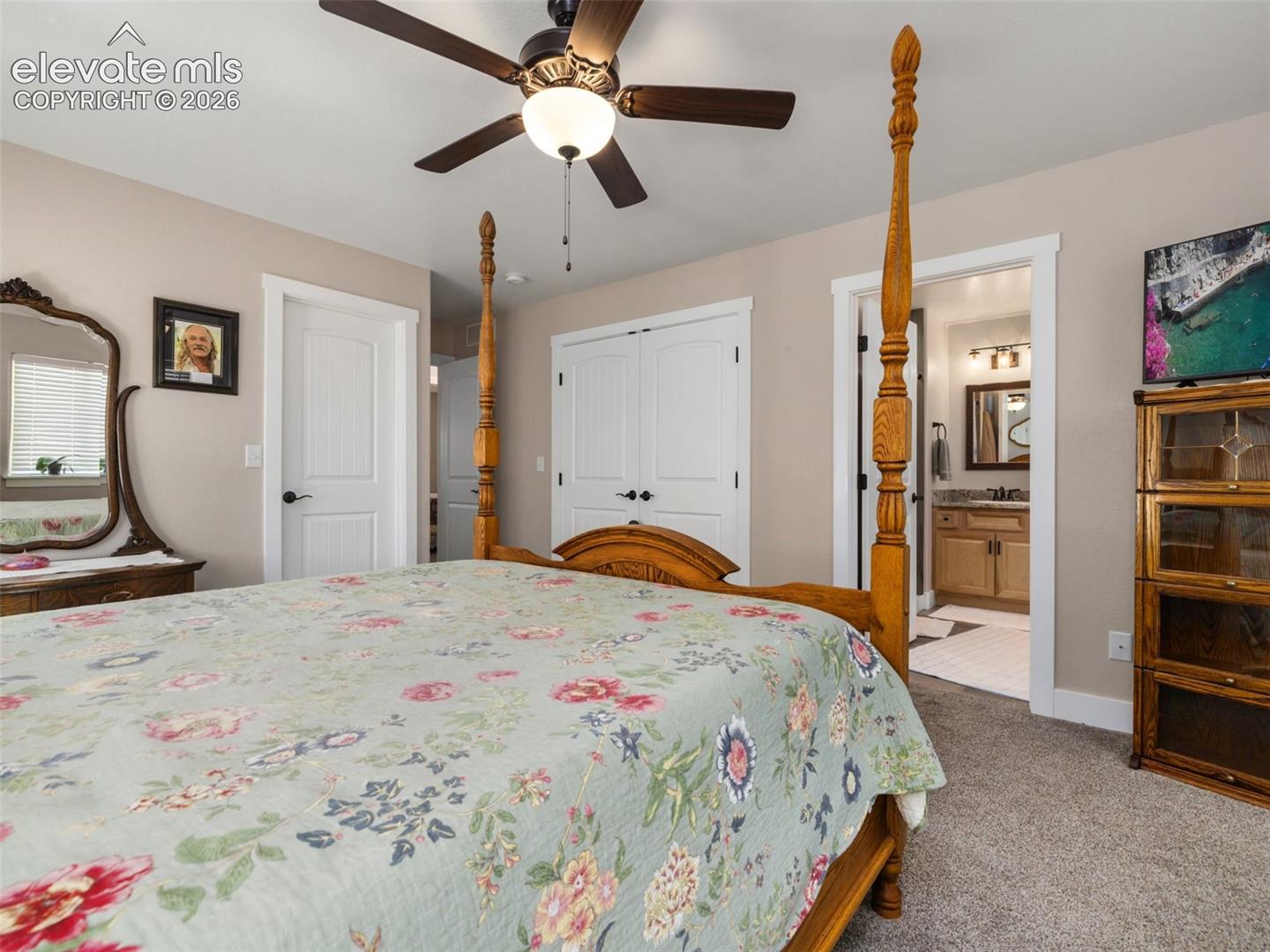 Ceiling fan with integrated lighting, wood-finish interior doors, neutral wall paint, carpeted flooring, and an adjoining room with vanity cabinetry and tiled flooring