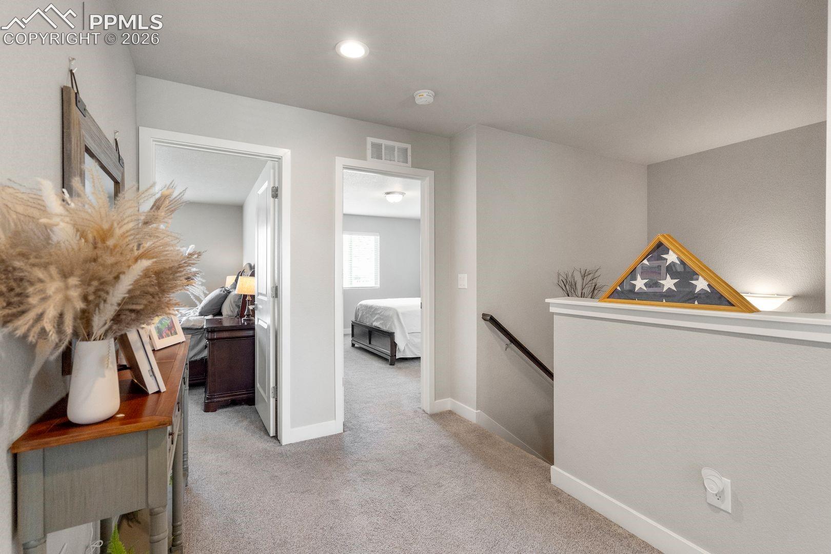 Corridor with light colored carpet and an upstairs landing