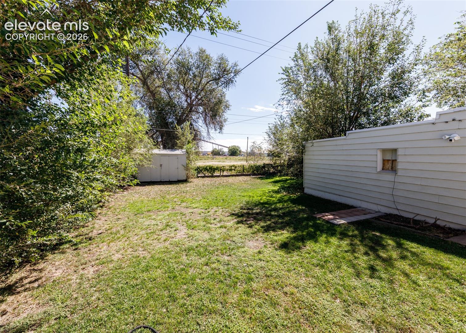 Expansive grassy area with established trees and a storage shed