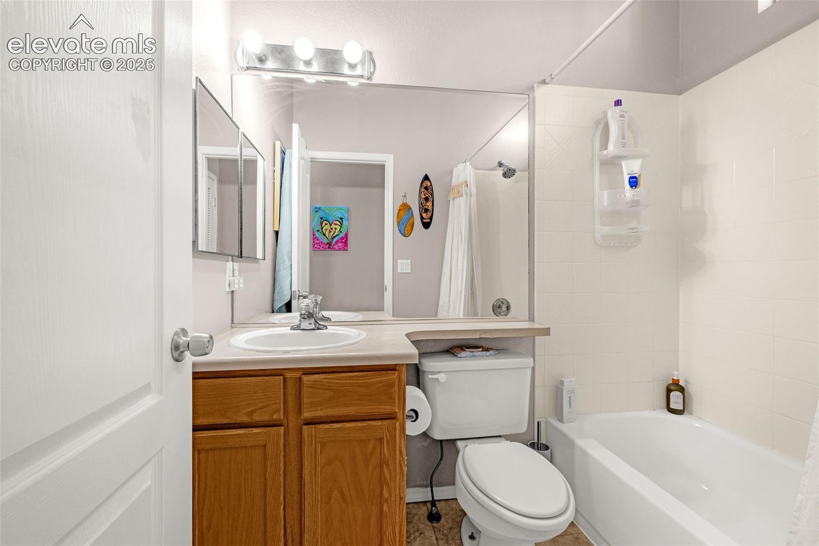 Bathroom featuring a wood-finish vanity, solid-surface countertop with an integrated basin, full-width wall mirror, three-light fixture, and a white tiled shower-tub combination