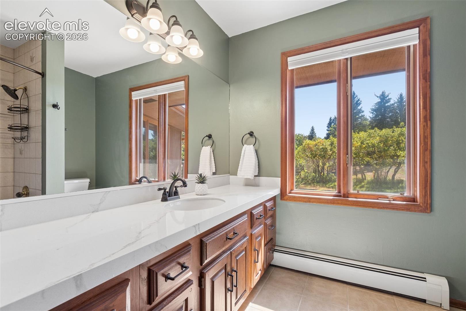 Dual basin vanity with a light-toned countertop, wood-finish cabinetry, and a large mirror