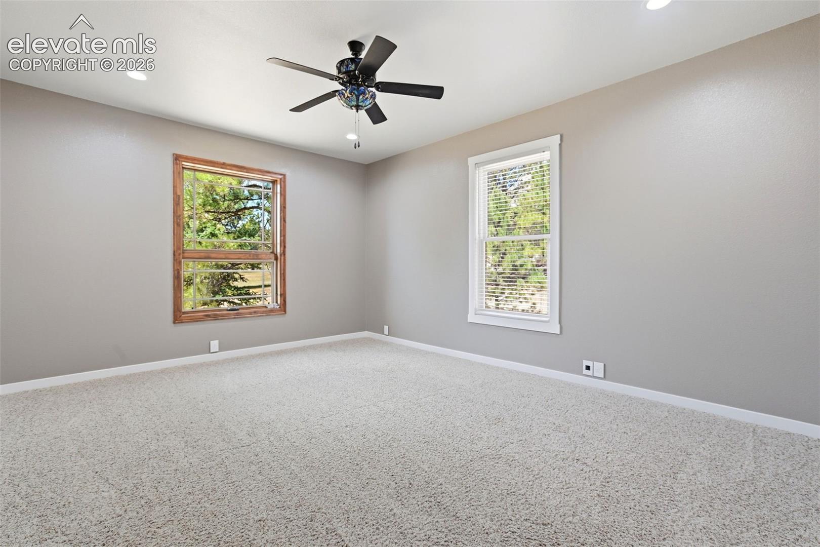 Spacious room featuring neutral carpeting, a ceiling fan with integrated lighting, recessed lighting, and two windows providing natural light