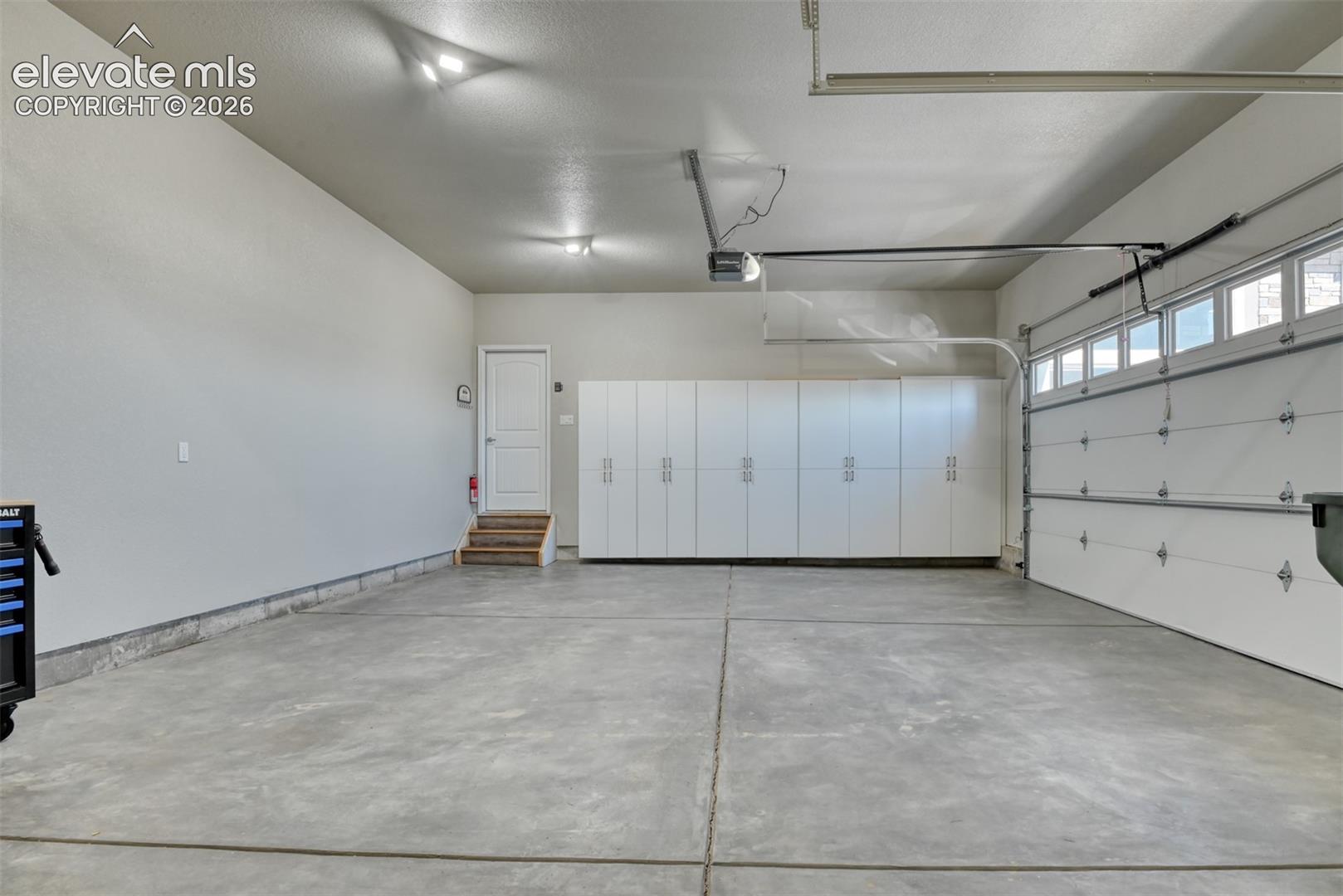Attached garage with concrete flooring, extensive built-in white cabinetry, an automatic garage door opener, and natural light from transom windows.