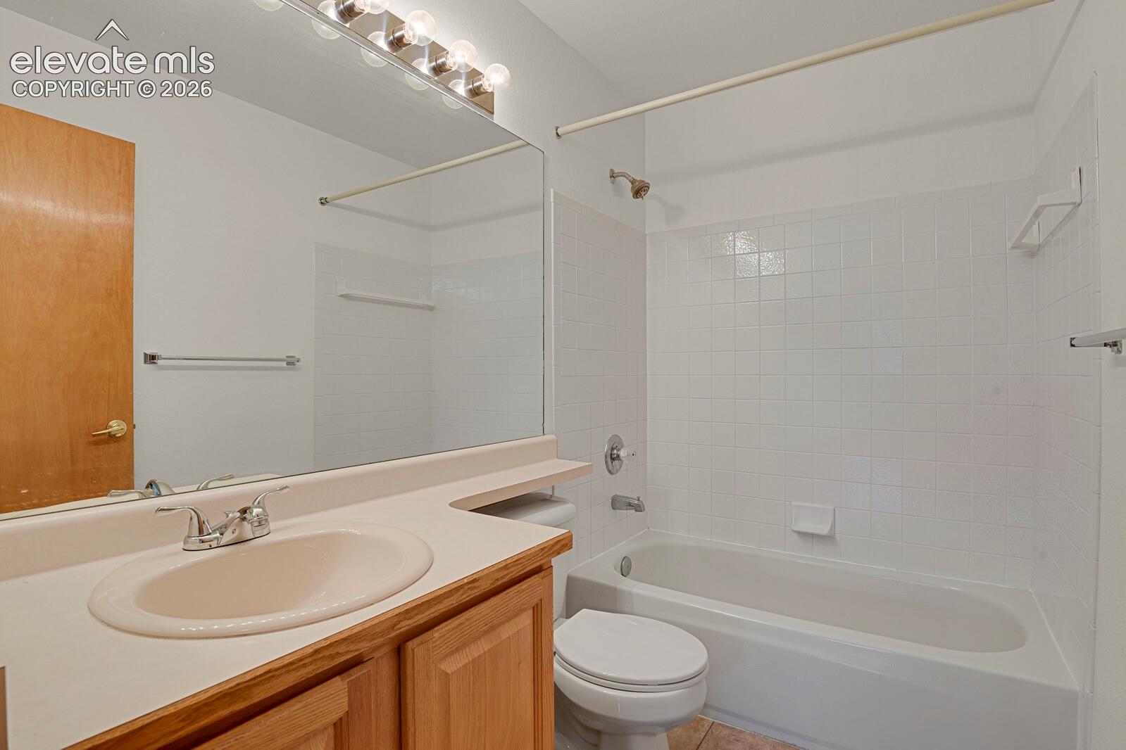 Bathroom featuring a single vanity with wood-finish cabinetry, a large mirror with integrated lighting, and a bathtub with white tile surround