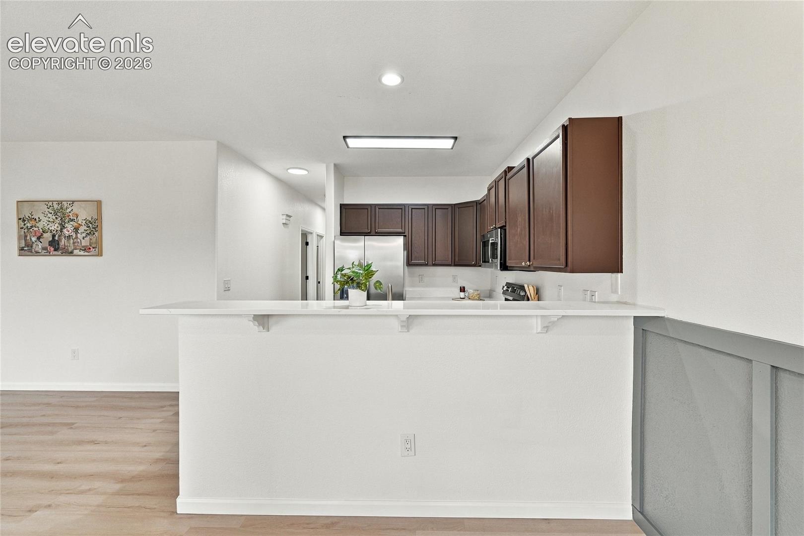 Kitchen featuring dark wood cabinetry, white countertops, stainless steel appliances, and a breakfast bar with panel molding