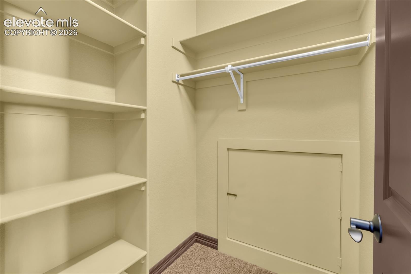 Storage area featuring wall-to-wall built-in shelving, a full-width hanging rod with support bracket, and an integrated access panel