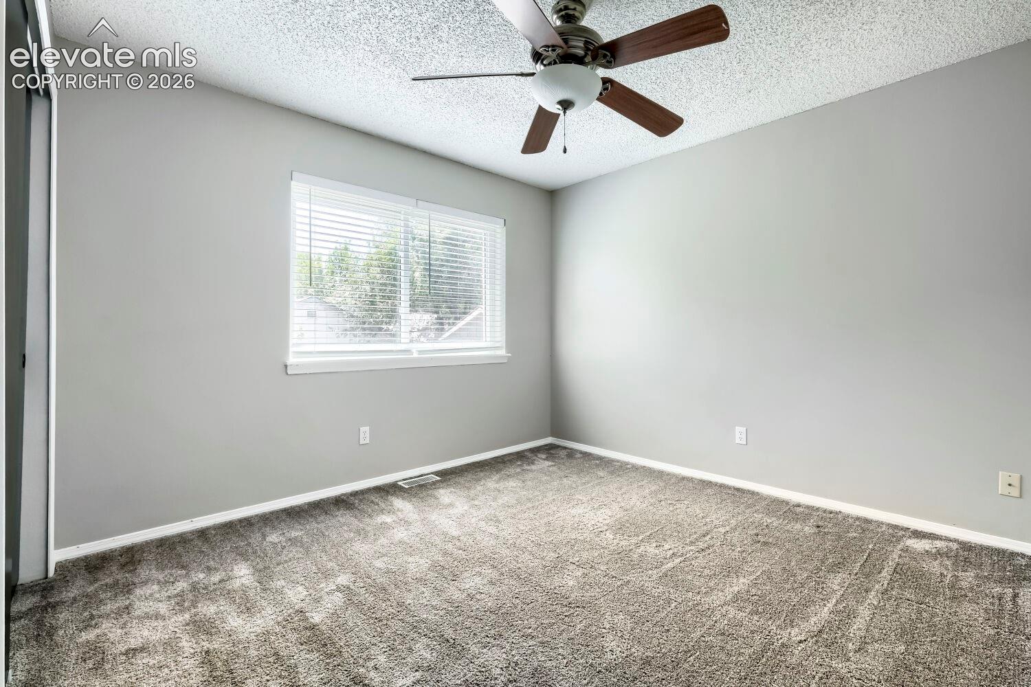Light gray walls complement the textured gray carpeting in this room featuring a window with horizontal blinds